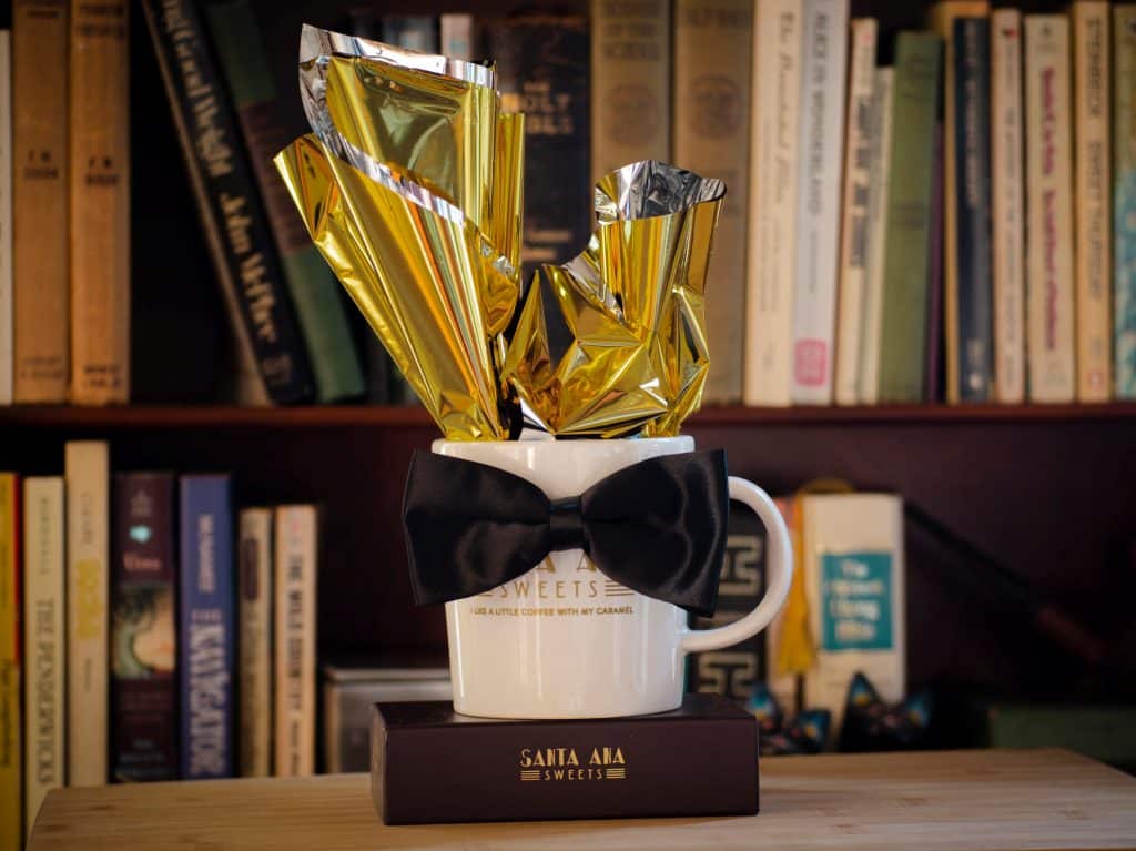 Santa Ana Sweets mug with a bow tie on top of a three piece box of caramels